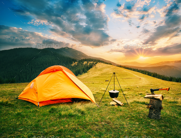 Tourist camp in mountains with tent and cauldron over fire at sunset